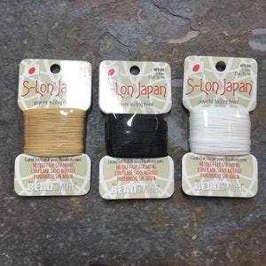 May include: Three spools of S-Lon Japan polyester beading thread. The spools are labeled with the brand name, thread type, and size. The thread colors are beige, black, and white.