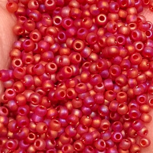 May include: A close-up view of a large quantity of small, round, red iridescent beads. The beads have a shiny, glossy finish and are perfect for jewelry making or crafting.