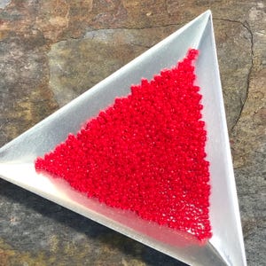 May include: A pile of small, bright red glass beads in a triangular silver tray.