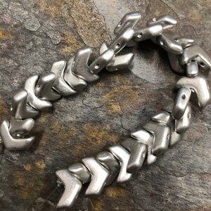 May include: A silver metal chain made of interlocking arrow-shaped beads.