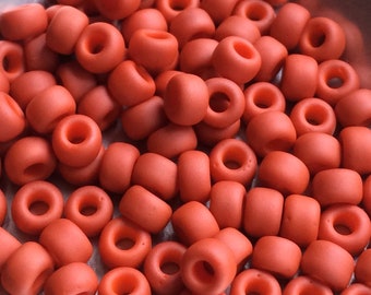 May include: A large pile of small, round, orange beads. The beads are made of glass and have a matte finish.