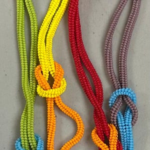 May include: A colorful beaded necklace with five strands of beads in different colors: yellow, green, orange, red, and blue. The strands are knotted together in a complex pattern.