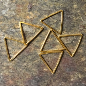 May include: A group of seven gold-colored triangle-shaped metal hoops. The hoops are arranged in a random pattern on a textured brown surface.