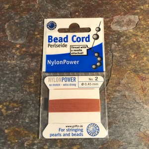 May include: A package of brown nylon bead cord, labeled "Bead Cord Perlseide NylonPower" with a needle attached. The package also says "No. 2 Ø 0.45 mm" and "For stringing pearls and beads".