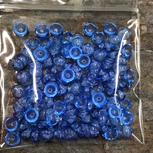 May include: A bag of blue glass beads with a frosted finish. The beads are small and round, and they have a slightly iridescent sheen.