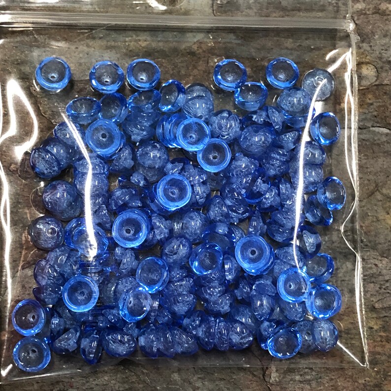 May include: A bag of blue glass beads with a frosted finish. The beads are small and round, and they have a slightly iridescent sheen.