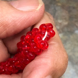 May include: A close-up of a red beaded necklace with a white string threaded through the beads.