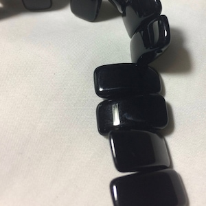 May include: A black onyx beaded necklace with rectangular beads. The beads are strung on a silver wire.