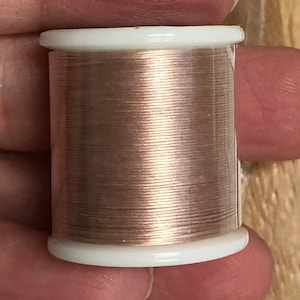 May include: A spool of metallic gold thread wound on a white plastic bobbin.