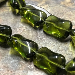 May include: A strand of dark green, faceted, glass beads. The beads are irregularly shaped and have a slightly cloudy appearance.
