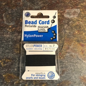 May include: A package of black NylonPower bead cord. The label reads "Bead Cord" and "Thread with a needle attached!" The cord is 2 meters long with a diameter of 0.75 mm. The packaging also states "For stringing pearls and beads."