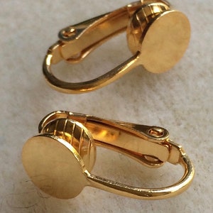 May include: A pair of gold-tone clip-on earrings. The earrings have a round, flat back and a spring-loaded clip.