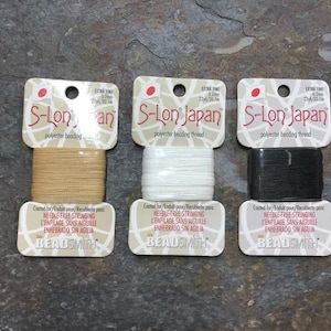 May include: Three spools of S-Lon Japan polyester beading thread. The spools are labeled "Extra Fine 0.2mm 22yd/20.1m" and are in the colors beige, white, and black.