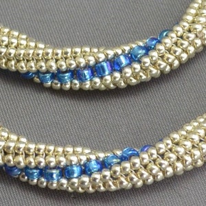 May include: A close-up of a silver and blue beaded necklace. The necklace is made with small, round beads and has a simple, elegant design.