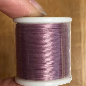 May include: A spool of mauve-colored thread in a clear plastic container with a white top.
