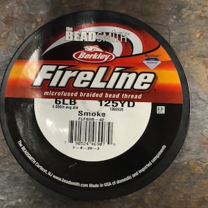 May include: A spool of Berkley FireLine microfused braided bead thread fishing line in smoke color. The spool is labeled with 6lb test, 125 yards, and 0.006in average diameter. The spool is black with a red and yellow label.