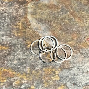 May include: A group of six silver jump rings, stacked and overlapping, on a textured brown and gold surface.