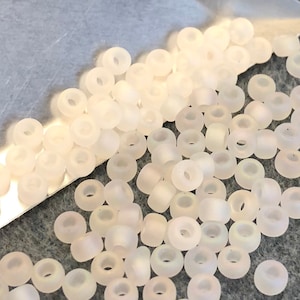 May include: A pile of small, white, opaque glass beads. The beads are round with a hole in the center.