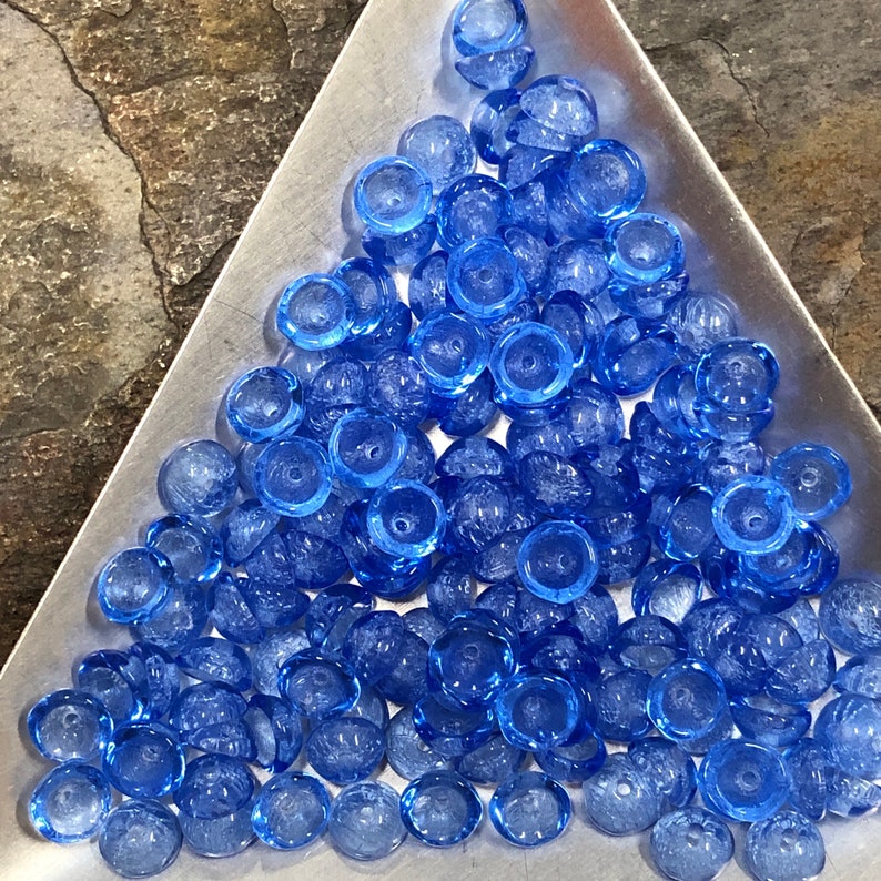 May include: A large group of blue glass beads with a textured surface. The beads are round and have a small hole in the center.