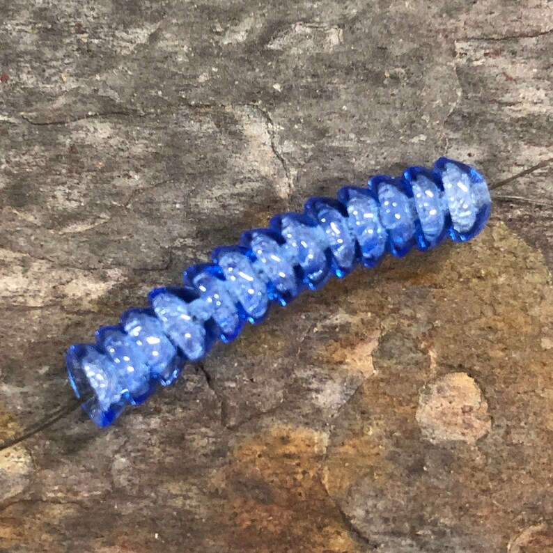 May include: A single blue glass bead with a textured, spiral design. The bead is strung on a thin wire.