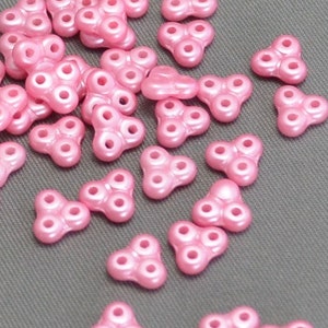 May include: A group of pink plastic beads with three holes each. The beads are shaped like a triangle with rounded edges.
