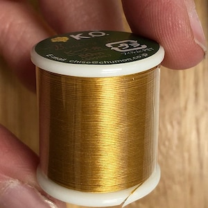 May include: A spool of gold-colored beading wire with a label that reads "KO Beading Wire 50m (series) Film & PET Email chiae@chumon.co.jp"