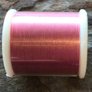 May include: A spool of pink thread wound on a white plastic bobbin.