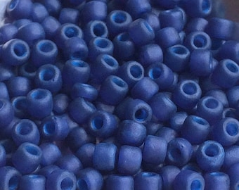 May include: A close-up image of a pile of small, round, blue glass beads. The beads have a matte finish and a slight iridescent sheen.
