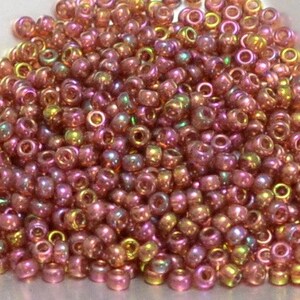 May include: A large pile of small, iridescent pink and gold seed beads. The beads are round and have a hole in the center.