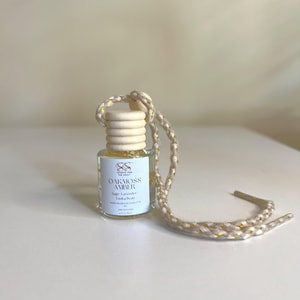May include: A small glass bottle with a wooden cap and a gold string. The bottle contains a clear liquid with gold glitter. The label on the bottle reads "Oakmoss Amber" and lists the scent notes as "Sage, Lavender, Tonka Bean".