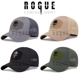 Może przedstawiać: Cztery czapki bejsbolowe w kolorze szarym, beżowym, czarnym i zielonym, każda z naszywką z czaszką. Czapki mają siateczkowe tyły i zakrzywione daszki. Tekst "ROGUE CONCEALMENT" jest widoczny nad czapkami.