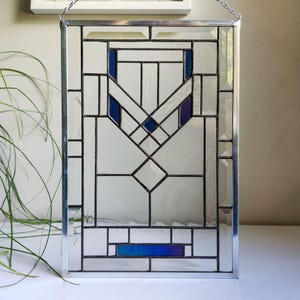 May include: A rectangular stained glass panel featuring a geometric pattern of clear glass panes framed in dark metal. The design includes symmetrical blue glass accents at the top and a single horizontal blue glass rectangle at the bottom base.