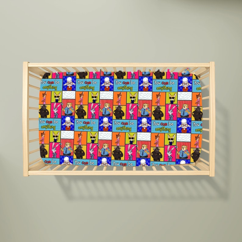 Puede incluir: Una s&aacute;bana de cuna con un patr&oacute;n de cuadr&iacute;cula repetitivo de personajes de dibujos animados de Zootopia, incluidos Judy Hopps y Nick Wilde, intercalados con el texto You can be anything en fuente amarilla sobre fondos rectangulares azules, naranjas y blancos.