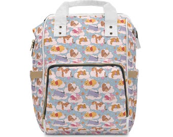 May include: A light blue backpack featuring a repeating pattern of Winnie the Pooh characters sleeping on white clouds with small pink and orange stars. The bag has white top handles, a front zippered pocket, and side pockets with tan accents.
