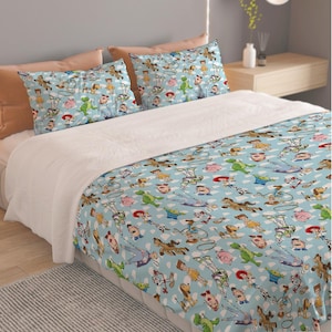 May include: A light blue bed set with a repeating pattern of cartoon characters, including a cowboy, a space ranger, and a green dinosaur. The set includes a duvet cover and two pillowcases.