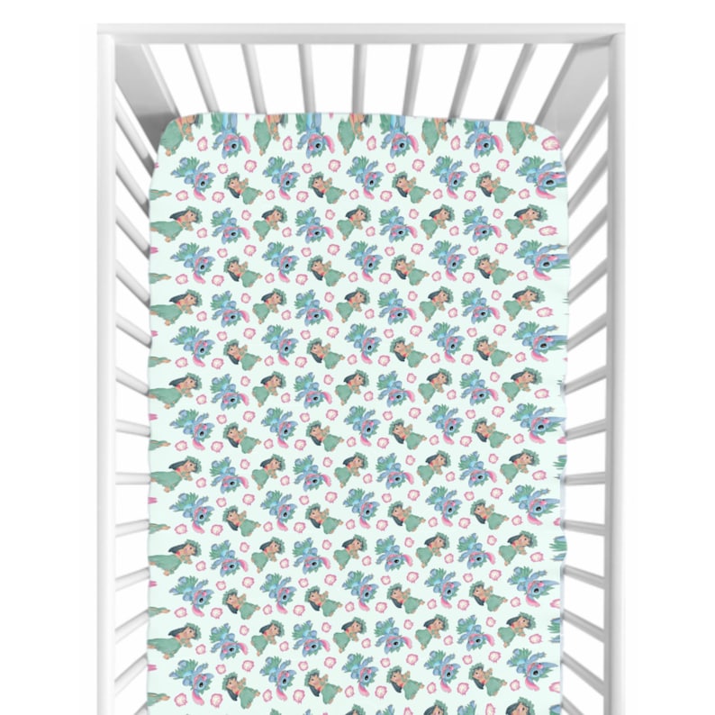 May include: A cot sheet featuring a repeating pattern of a cartoon character in blue, green, and pink on a pale green backdrop. The sheet is inside a white cot.