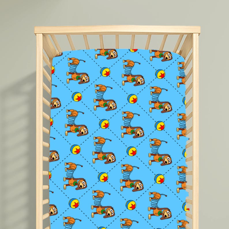 May include: A light blue cot sheet featuring a repeating pattern of brown dachshunds with blue spring bodies and colourful balls. The design is arranged in a diamond grid created by small dark blue dots, covering the entire surface of the fabric.