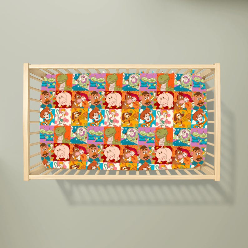 May include: A cot sheet featuring a repeating grid pattern of Toy Story characters including Woody, Buzz Lightyear, Rex, Hamm, Mr. Potato Head, Bo Peep, Slinky Dog, and the green aliens, set against a light-coloured wooden cot frame.