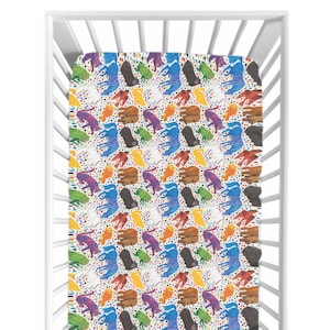 Puede incluir: Una sábana bajera para cuna con un colorido estampado de orugas ilustradas en varios colores, incluyendo azul, verde, marrón y morado, sobre un fondo blanco con pequeños puntos de colores. La sábana está dentro de una cuna blanca.