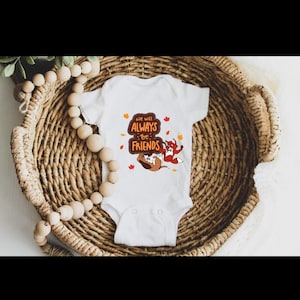May include: White baby onesie featuring an illustration of a fox and a hound dog. The onesie has the text "We will always be friends" with autumn leaves surrounding the text.