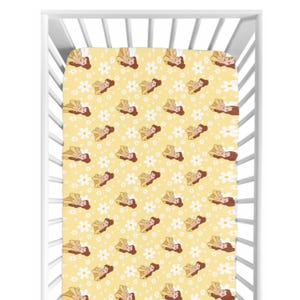 Puede incluir: Una sábana bajera ajustable amarilla con un estampado repetido de una princesa de dibujos animados y margaritas blancas. La princesa lleva un vestido amarillo y tiene el pelo castaño. La sábana está dentro de una cuna blanca.