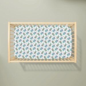 May include: A light blue cot sheet featuring a repeating pattern of a cartoon character in blue, green, and pink. The cot sheet is inside a wooden cot frame.