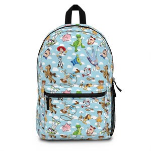 Op de afbeelding: Een lichtblauwe rugzak met een all-over print van diverse geanimeerde speelgoedfiguren, waaronder een cowboy, een cowgirl, een space ranger, een dinosaurus, een varken en een vorkfiguur, tegen een achtergrond van witte wolken en zwarte ritsen.