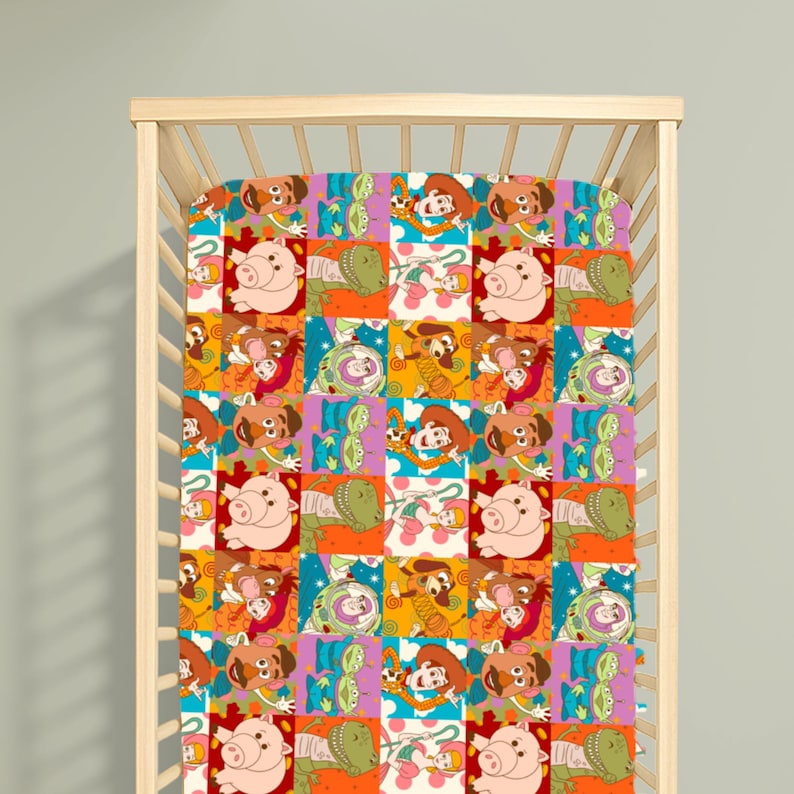 May include: A cot sheet featuring a repeating grid pattern of Toy Story characters including Woody, Buzz Lightyear, Jessie, Mr. Potato Head, Hamm, Rex, and the green aliens. The design uses vibrant colours like orange, pink, blue, and yellow squares.