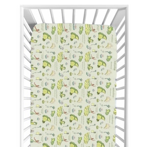 May include: A fitted crib sheet with a repeating pattern of whimsical illustrations. The design features figures in yellow dresses, green frogs, and floral elements on a light green background. The sheet is displayed inside a white crib.
