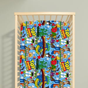 May include: A light blue cot sheet featuring a repeating pattern of Toy Story characters including Buzz Lightyear, Woody, and Slinky Dog, along with text elements like Toy Story Mania, Sarge Says, and Let's Play, set against a colourful graphic background.