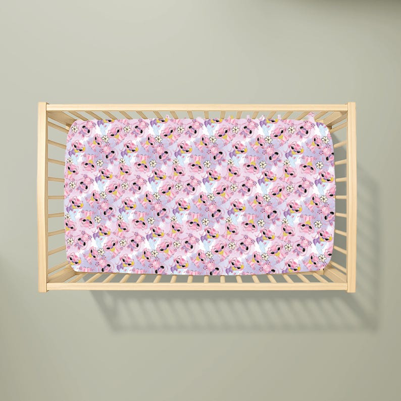 May include: A crib sheet with a repeating pattern of a cartoon character in pink, purple, and white. The sheet is inside a wooden crib frame. The cartoon character has large eyes and a flower on its head. The background is a light purple color.