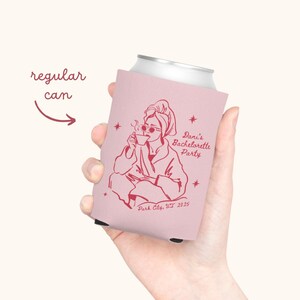 May include: A pink can cooler featuring a red illustration of a person in a robe and sunglasses, holding a cup. Text on the cooler reads "Dani's Bachelorette Party, Park City, UT 2025". The cooler is designed for a regular can.