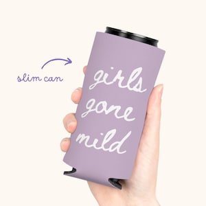May include: A lavender slim can cooler with the words "girls gone mild" in white script. The cooler is designed to hold a slim can and is held in a person's hand.