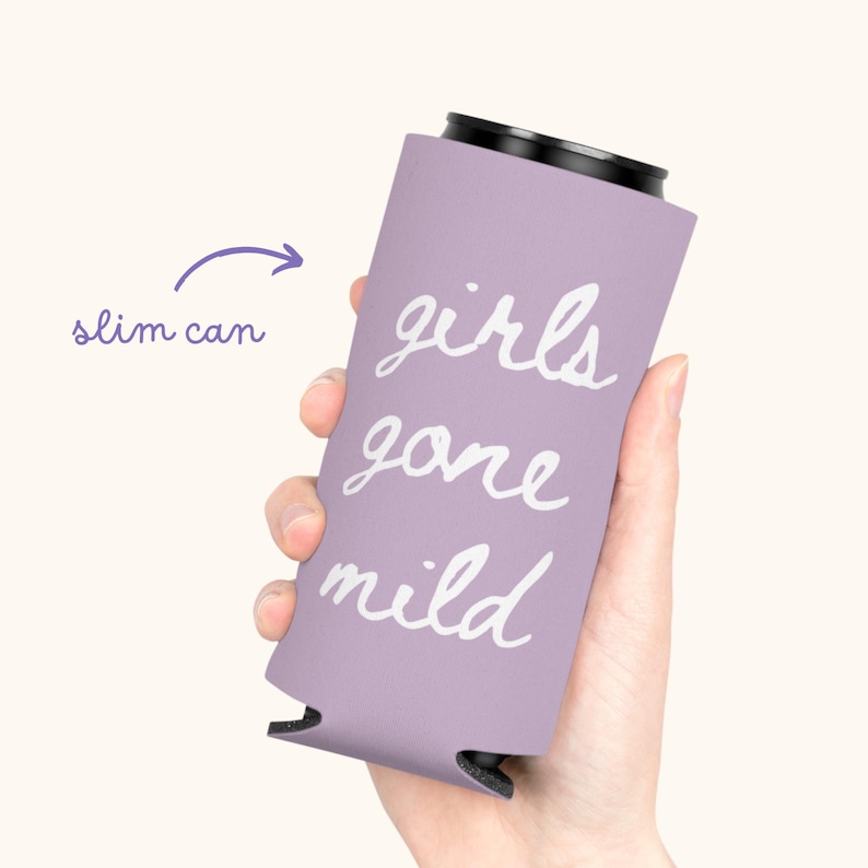 May include: A lavender slim can cooler with the words "girls gone mild" in white script. The cooler is designed to hold a slim can and is held in a person's hand.